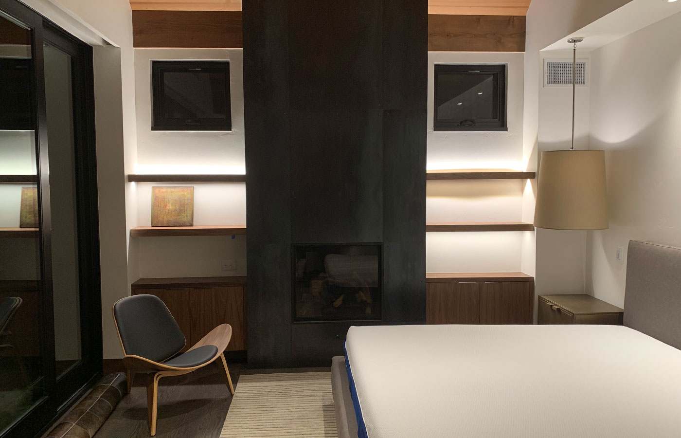 sleek bedroom with striking, modern black fireplace and built-in shelving